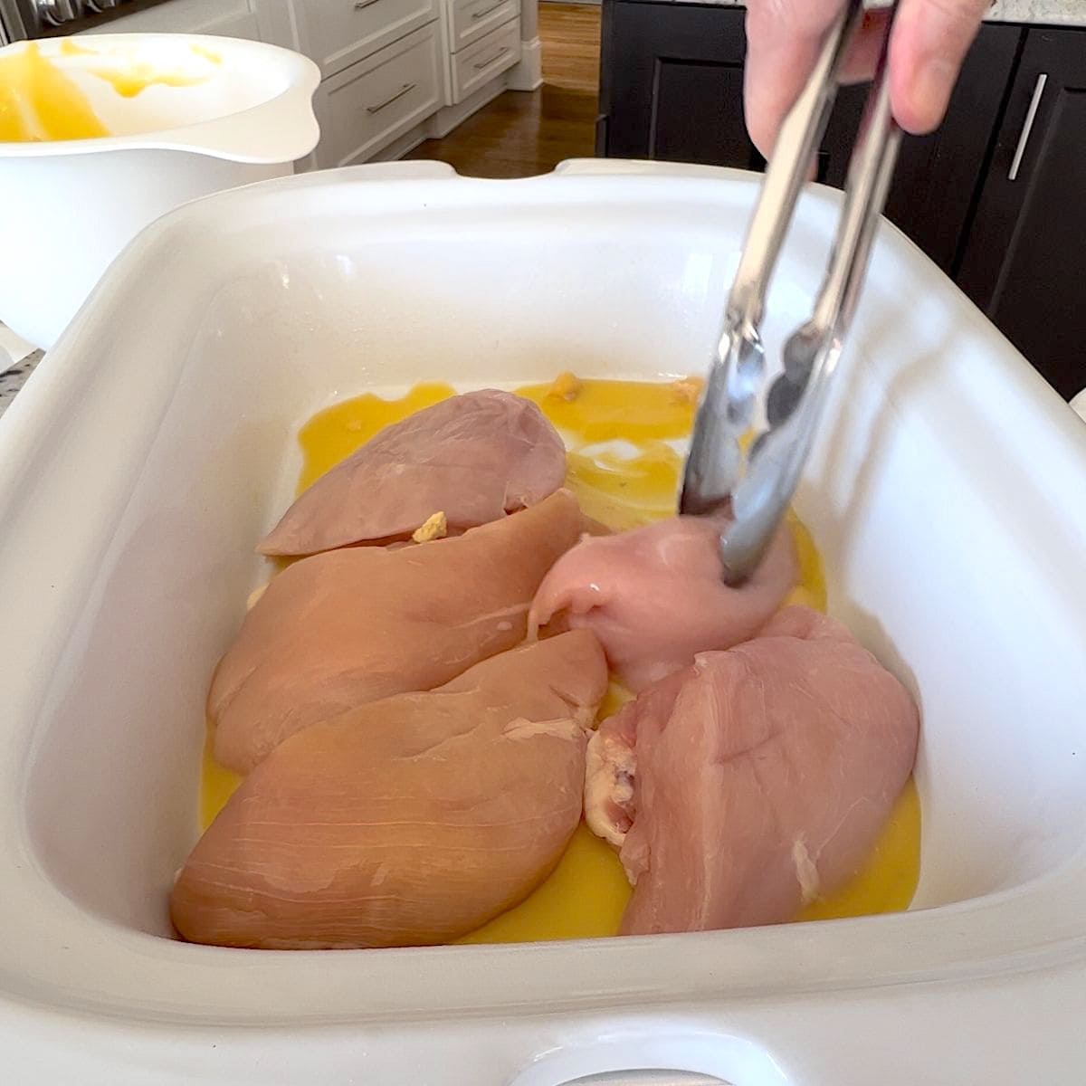 Placing the chicken breasts in a white rectangle crock pot.