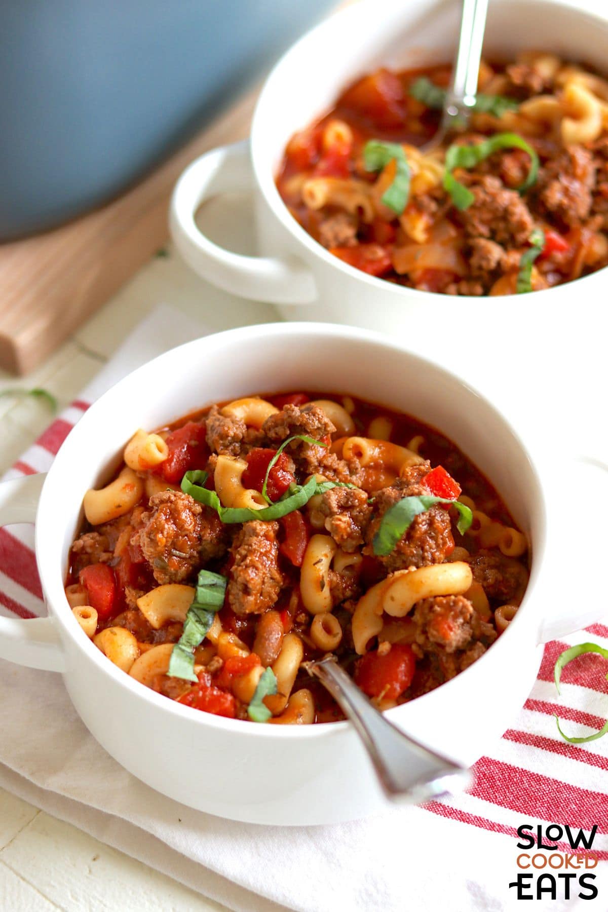 Two bowls of slow cooker American goulash served with spoons.