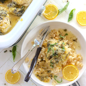 A round white bowl full of sunny lemon pepper chicken over risotto with a slice of lemon.