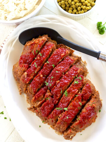 Slices of crock pot meatloaf served on a white platter with a topping of ketchup and brown sugar.