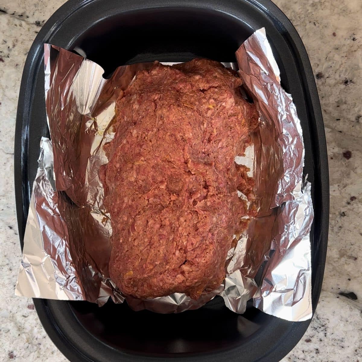 A shaped meat loaf in a black oval crock pot.