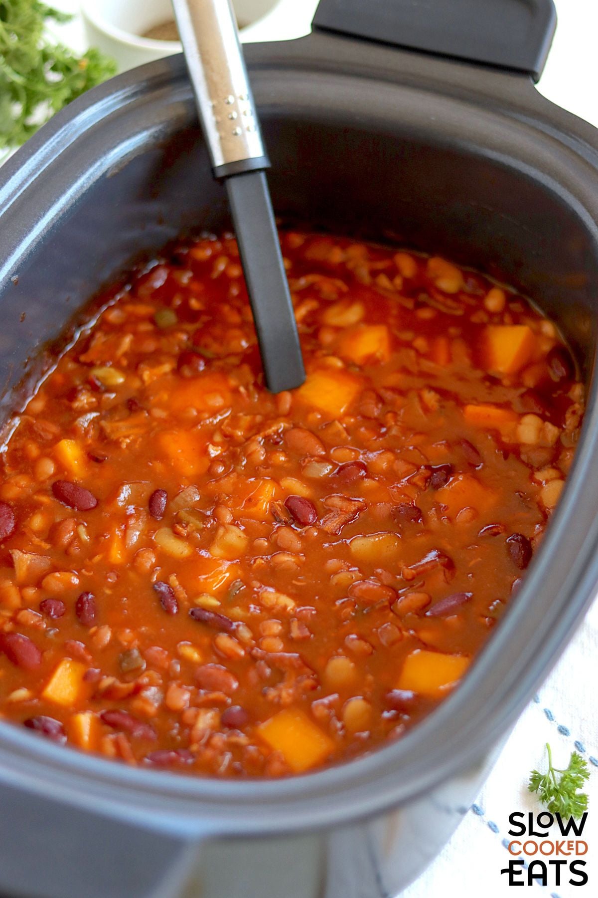 Easy slow cooked baked beans with bacon with spoon for scooping.