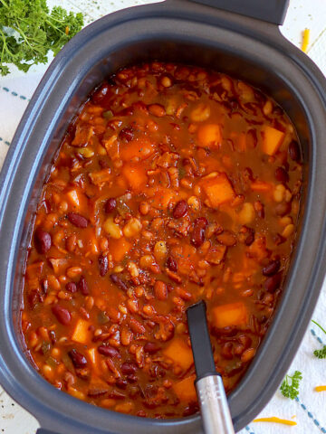 A spoon in a black crock pot of baked beans ready for serving.