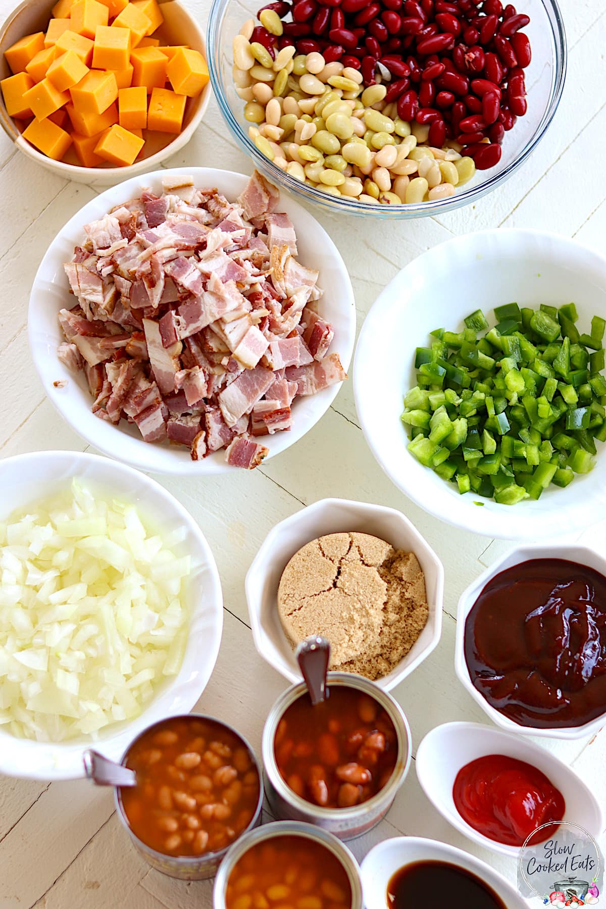 Ingredients needed for making crock pot baked beans with bacon on a white board.