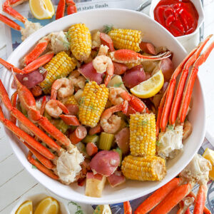 Seafood boil served on a large white platter with corn, sausage, shrimp, crab, potatoes, lemon wedges.