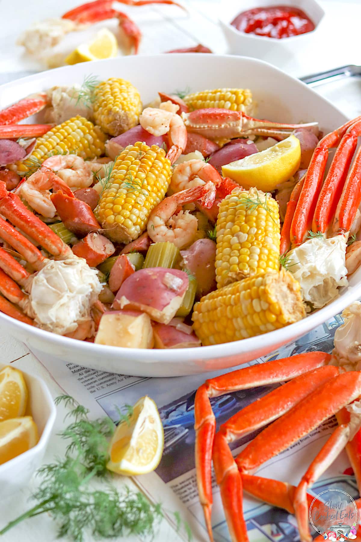 Crock pot seafood boil served in a large white platter with lemon wedges and fresh dill.
