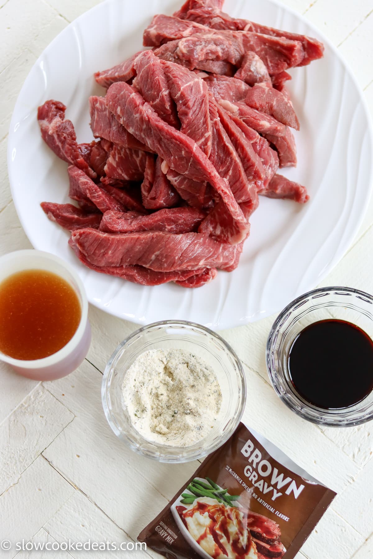 5 ingredients for making crock pot sirloin steak laying on a white wooden table.