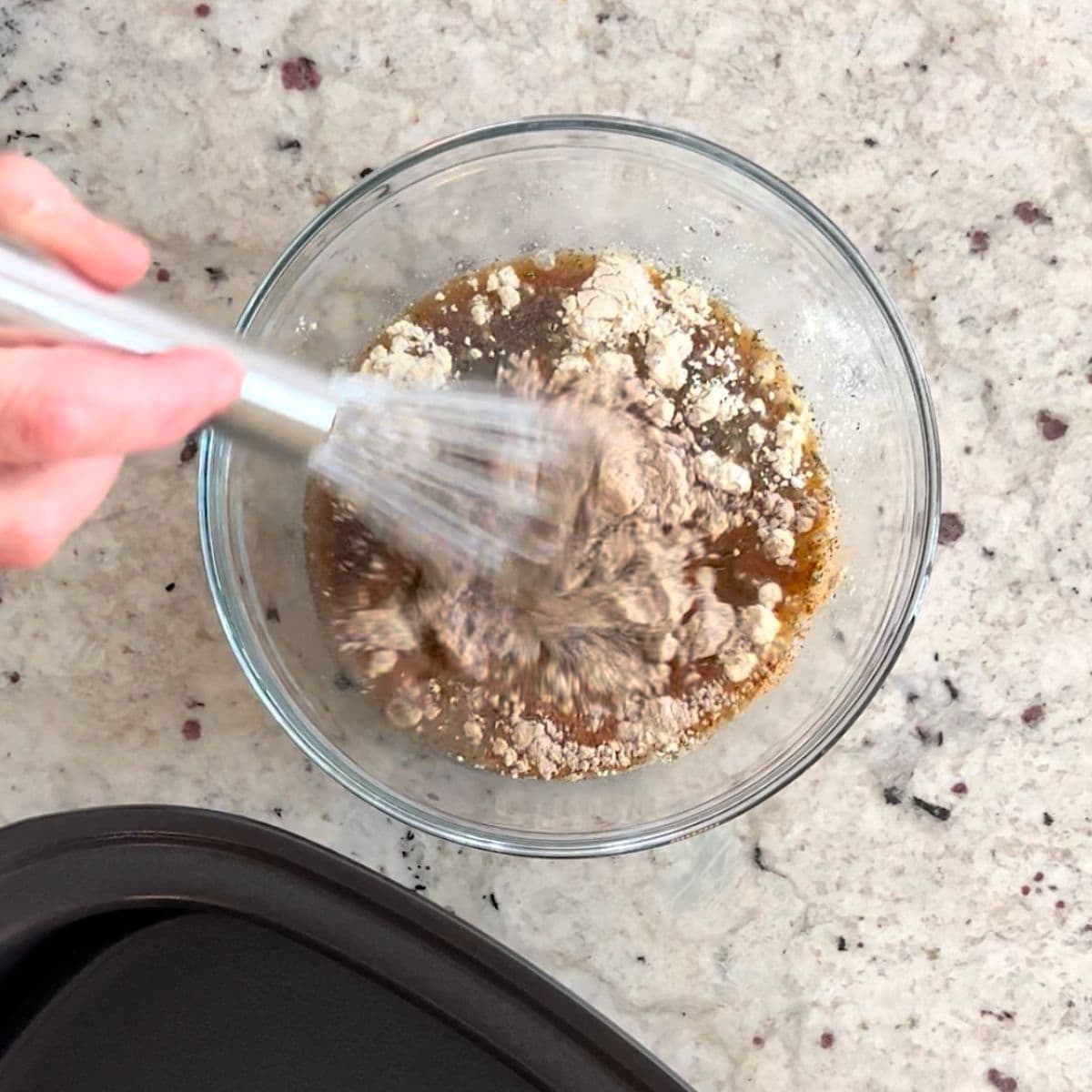 Whisking the sauce and seasoning in a clear glass bowl.
