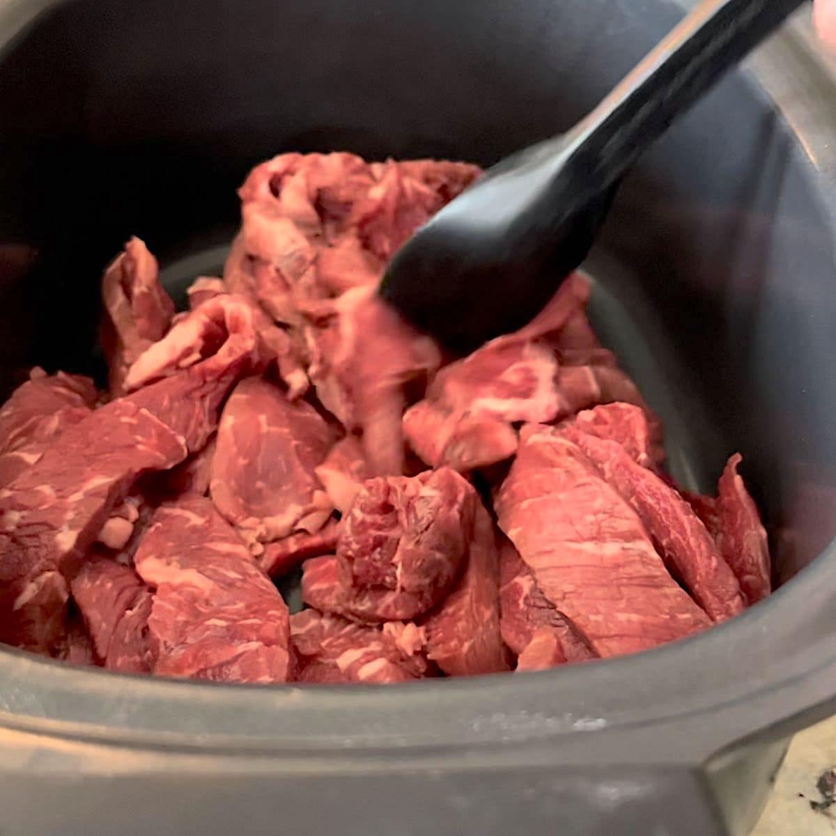 Placing the sirloin steak slices in the crock pot.