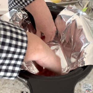 Lining a black crock pot with foil for lifting the cake.