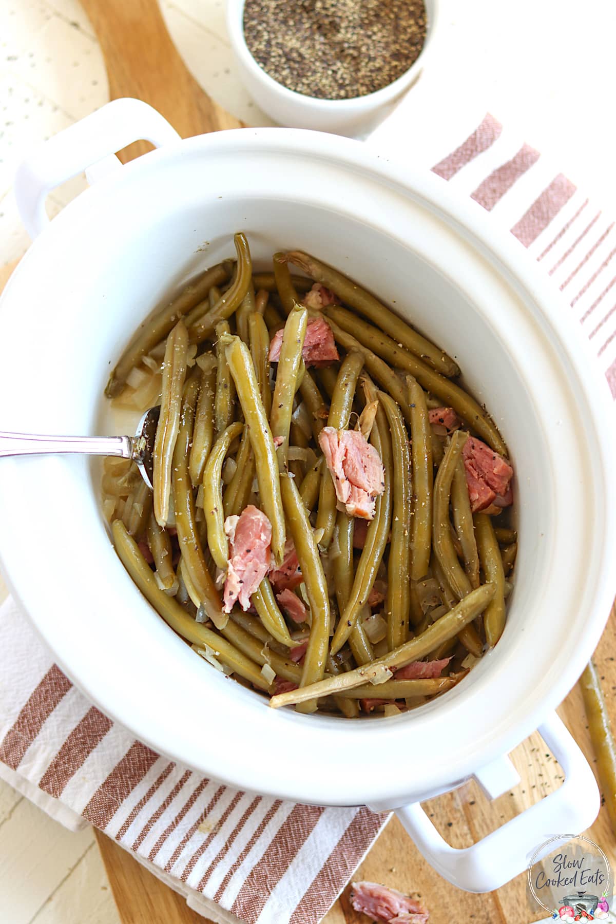 Crockpot green beans with ham in a slow cooker with ham chunks and onion bits. 