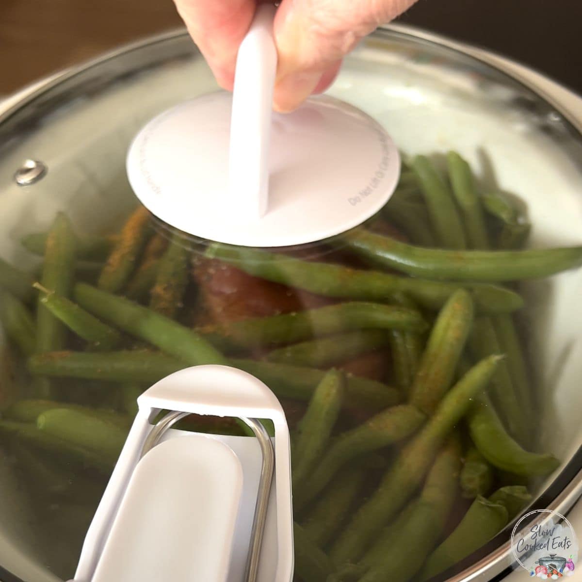 Covering a crock pot of green beans with a clear glass lid.