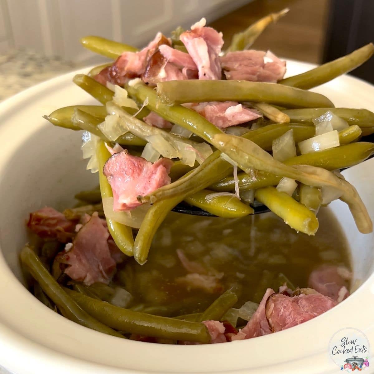 Draining the liquid from the crockpot green beans and ham.