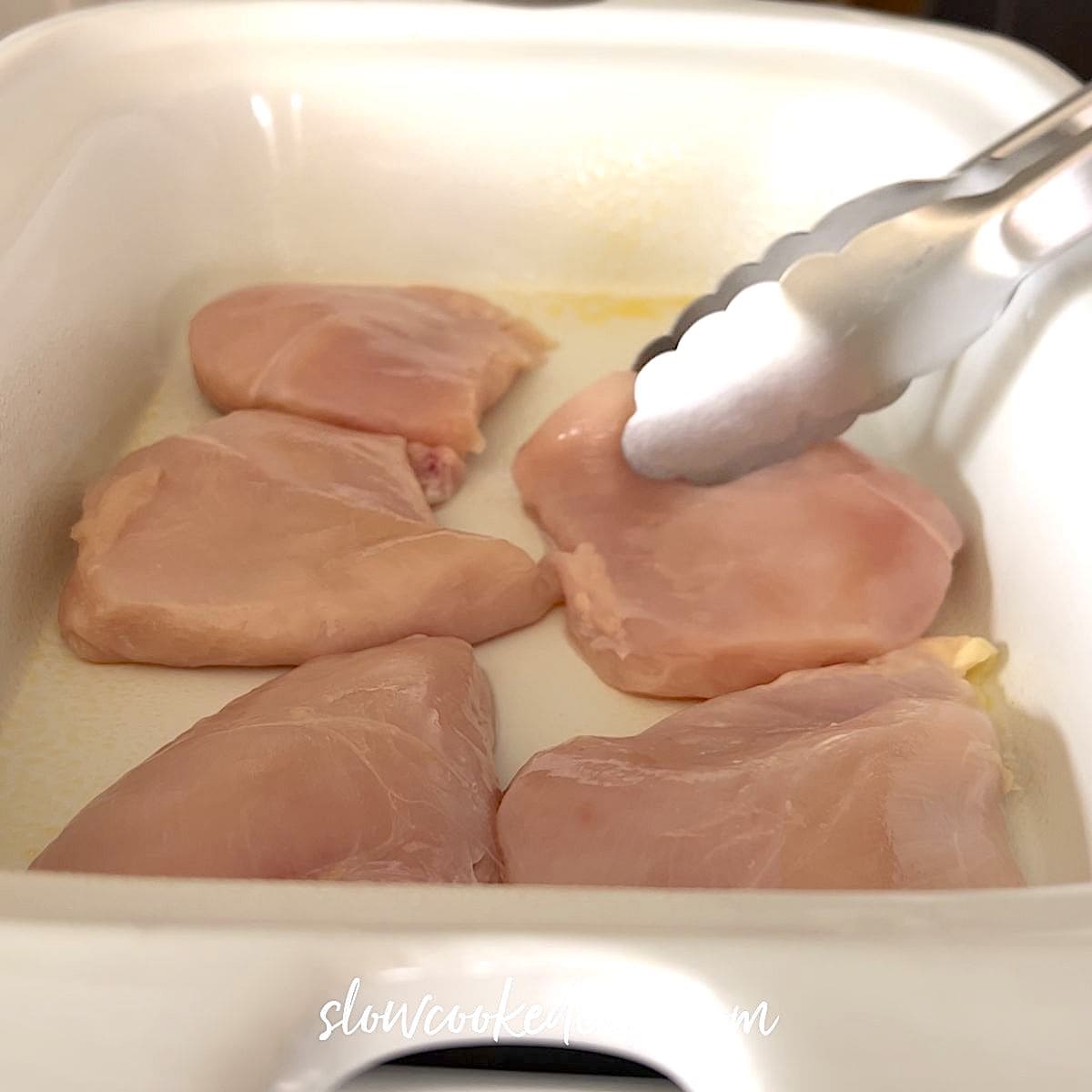 Placing the chicken breasts on the bottom of a white crock pot.