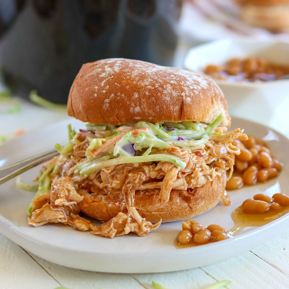 A gray plate with pulled chicken on a bun with coleslaw and a side of baked beans.