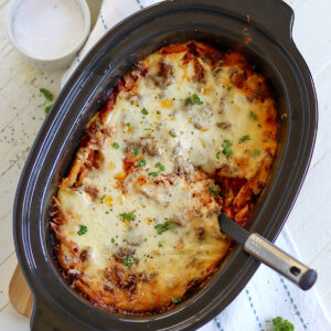 Baked ziti in a black oval slow cooker with handles.