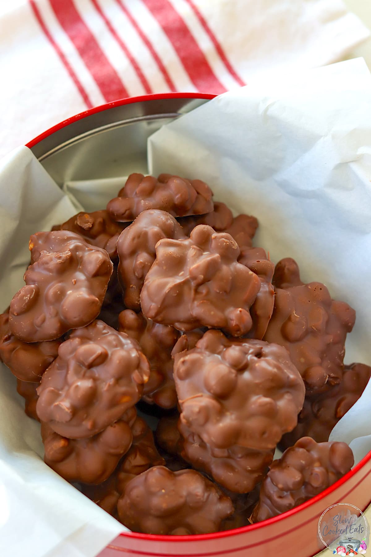 Crock pot peanut clusters in a red tin lined with parchment paper.