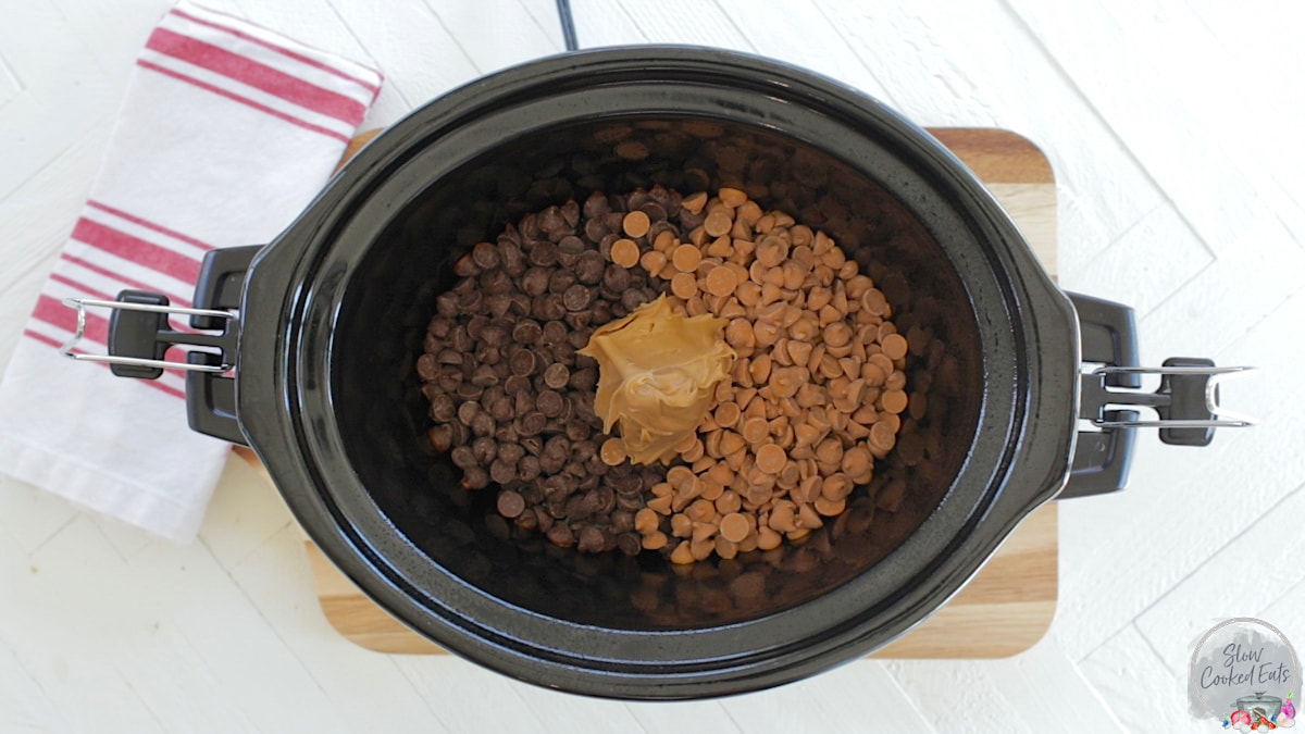 Adding chocolate chips, butterscotch chips, and peanut butter into a small oval black crock pot.
