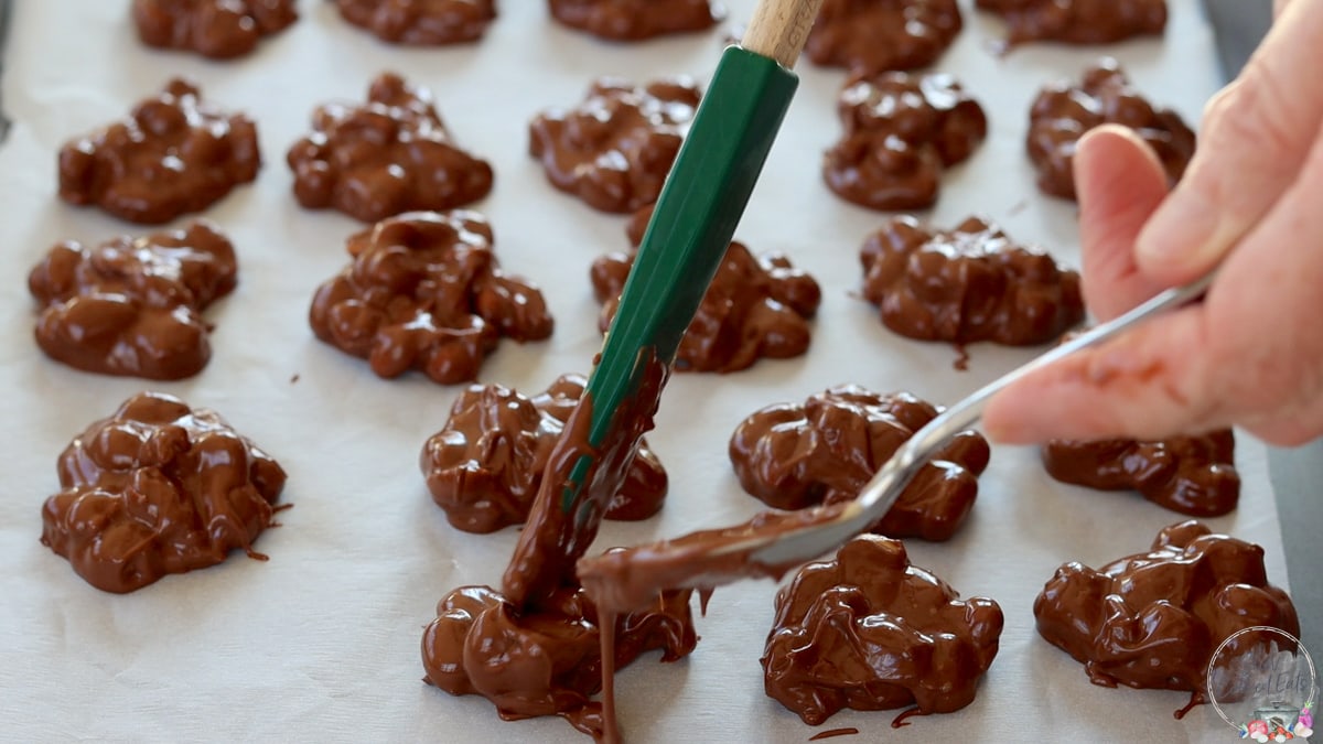 Dropping peanut clusters by the spoonful on a parchment lined tray.