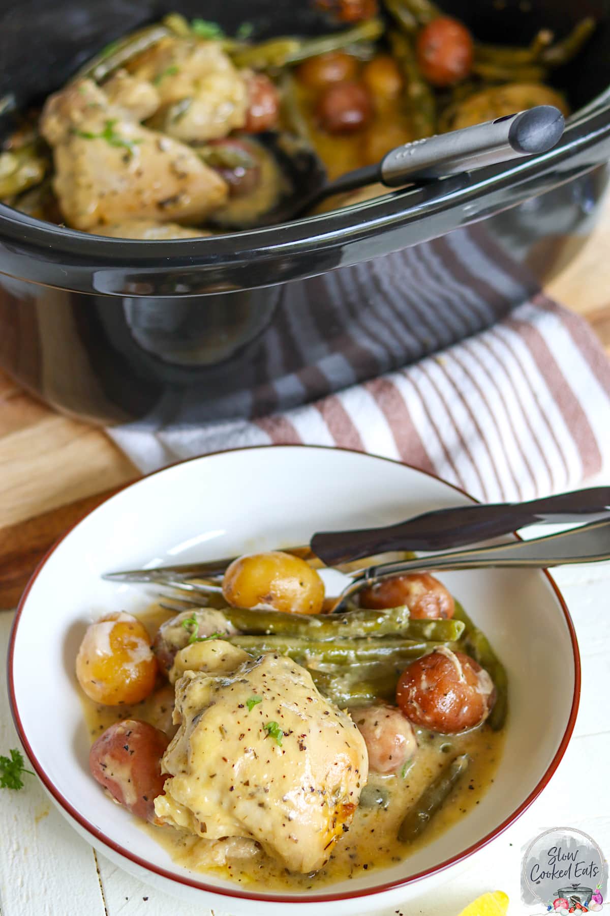 A round white shallow bowl with a serving of chicken potatoes and green beans.