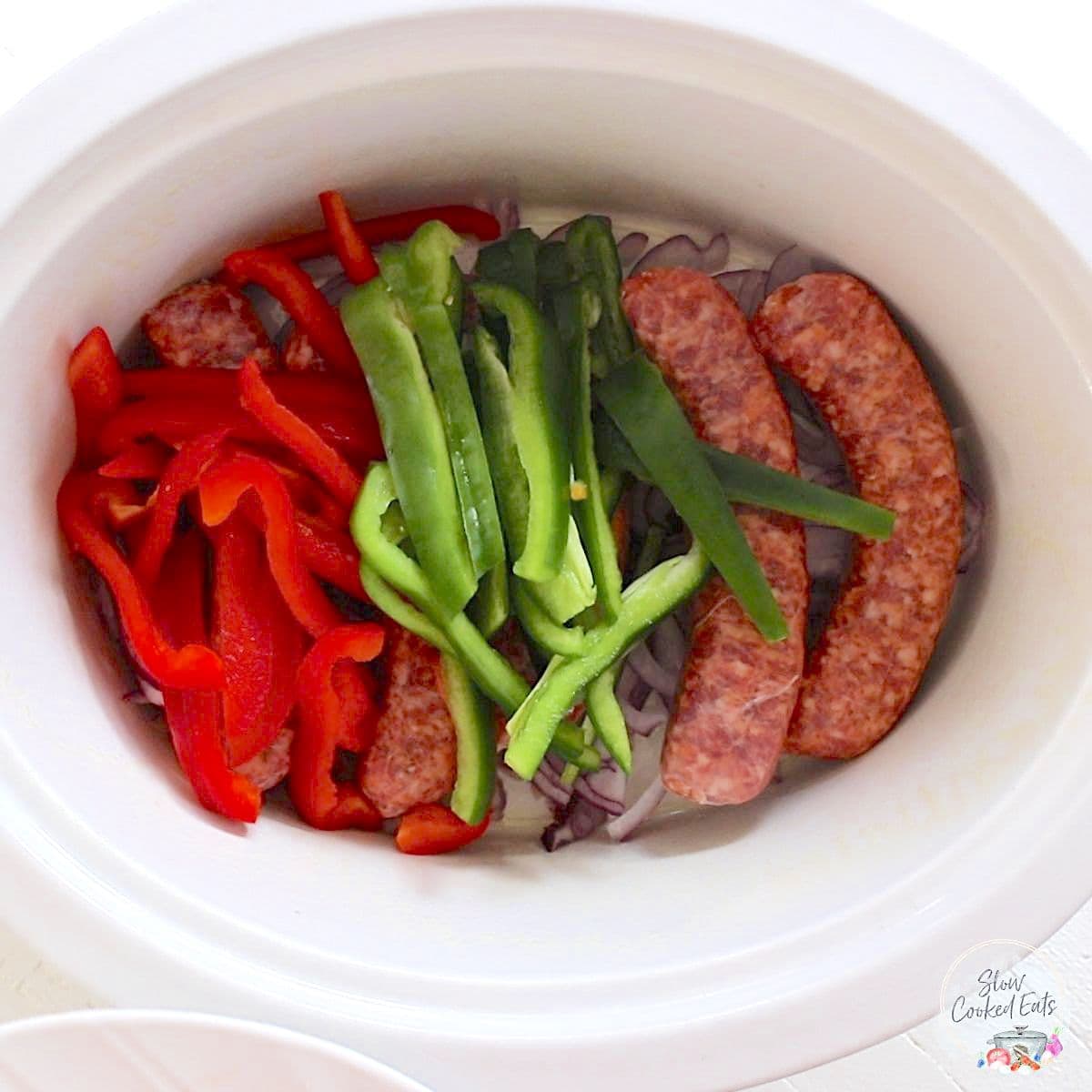 Adding the Italian sausages, bell peppers, and onion in a white crock pot.