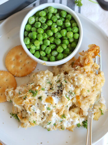 chicken and green peas served on a white plate with crackers.