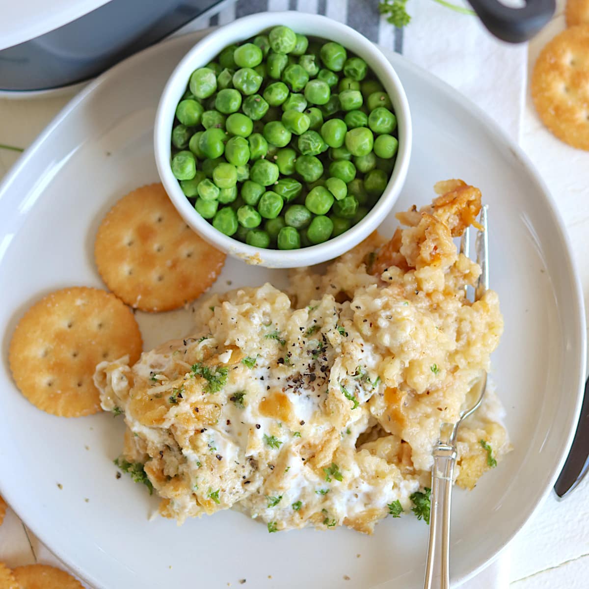 chicken and green peas served on a white plate with crackers.