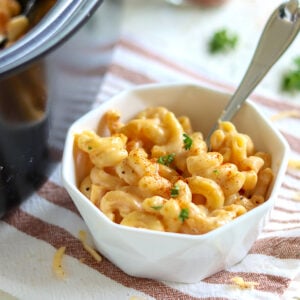 White porcelain bowl filled with macaroni and cheese. Garnished with a sprinkle of fresh chopped herbs and seasoning.