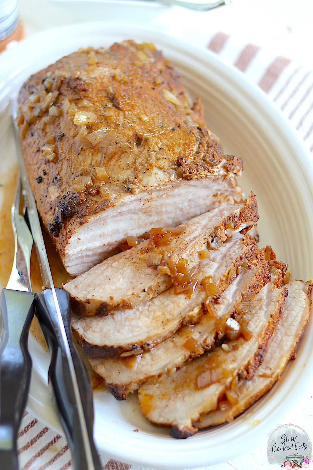 A juicy slow cooked and sliced pork loin on an oval white plate.