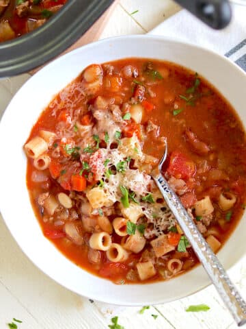 A white bowl full of pasta fagioli with a spoon.