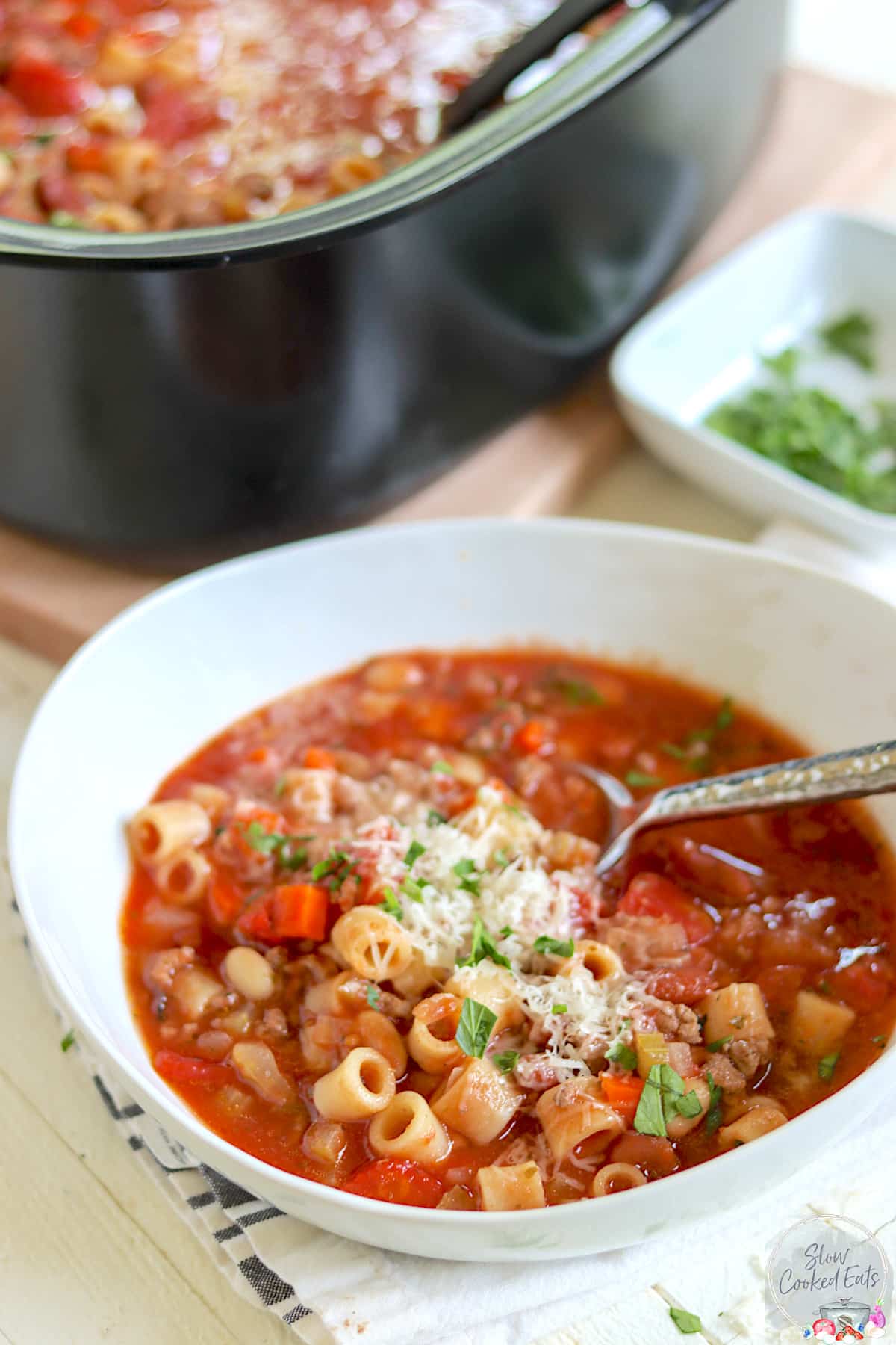 A white bowl and a black slow cooker full of pasta fagioli.