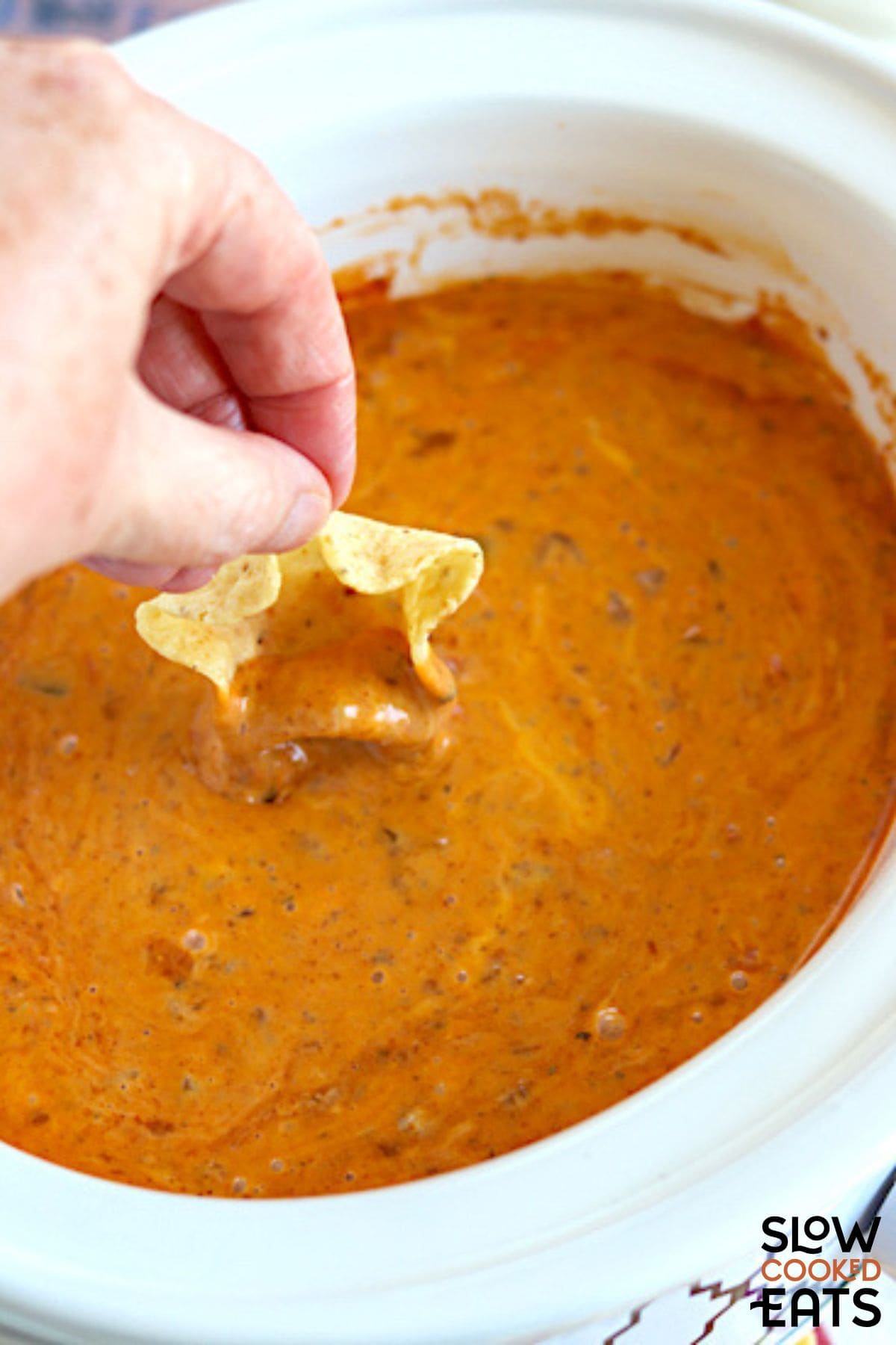 Crockpot rotel dip being scooped with a tortilla chip.