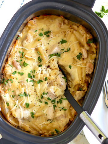 Crock pot chicken alfredo with melted cheese and fresh parsley in an oval crock pot.