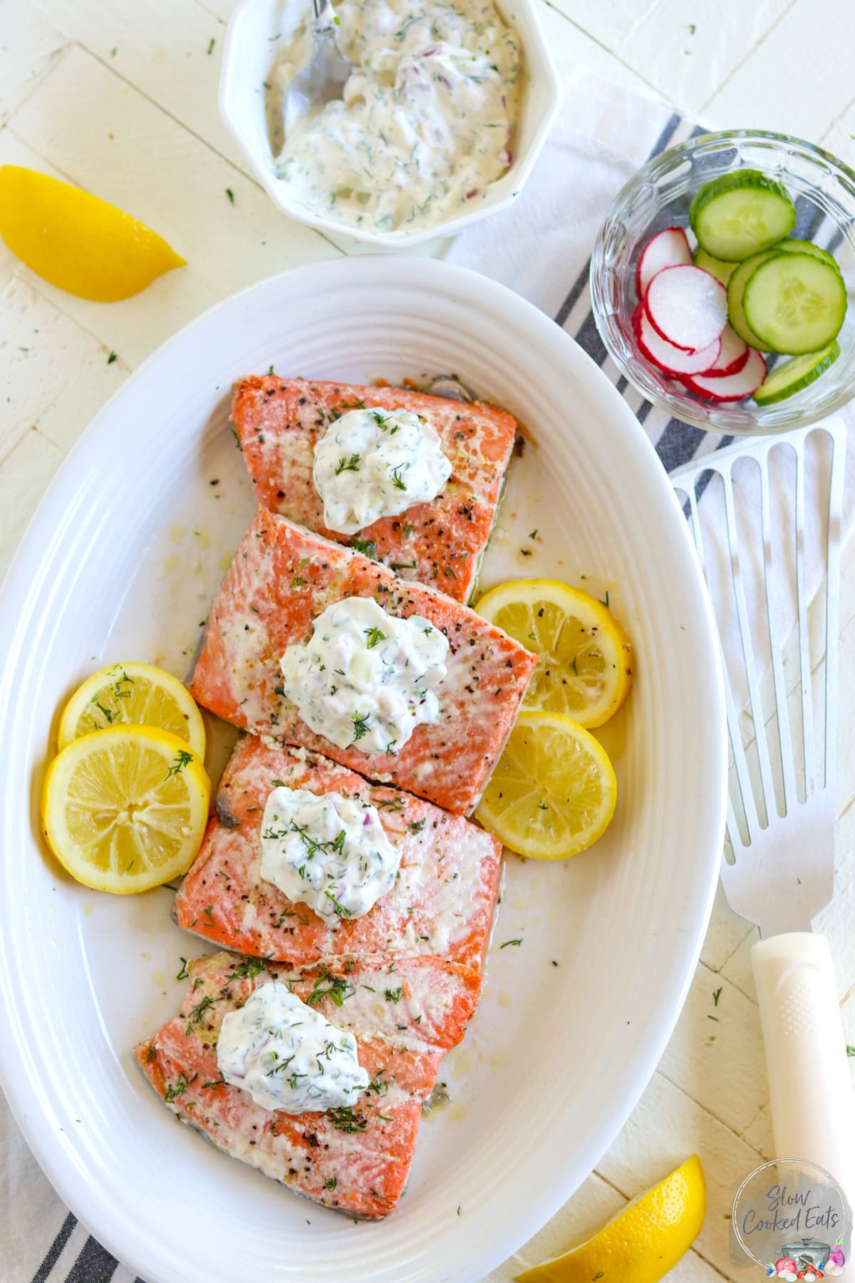 Poached salmon on a white oval platter topped with dill sauce and slices of lemon.