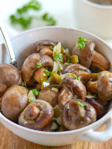 A round white bowl of crockpot ranch mushrooms garnished with fresh parsley.