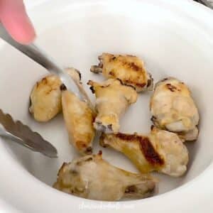 Adding the chicken wings to a white crock pot.