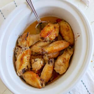 A white oval crock pot full of cooked honey garlic wings.
