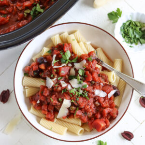 A white bowl of puttanesca sauce serve over rigatoni pasta.