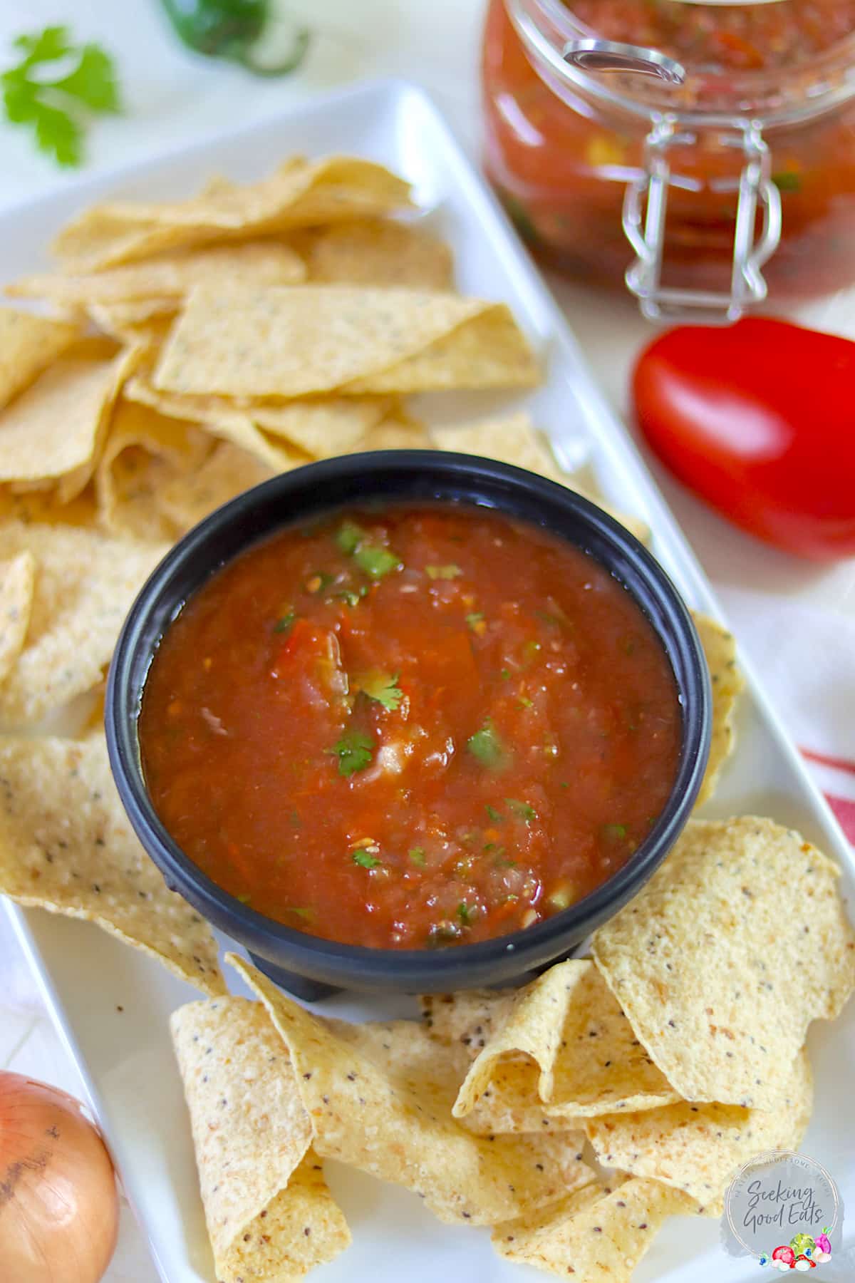 A white tray with tortilla chips scattered around a black bowl of red salsa.