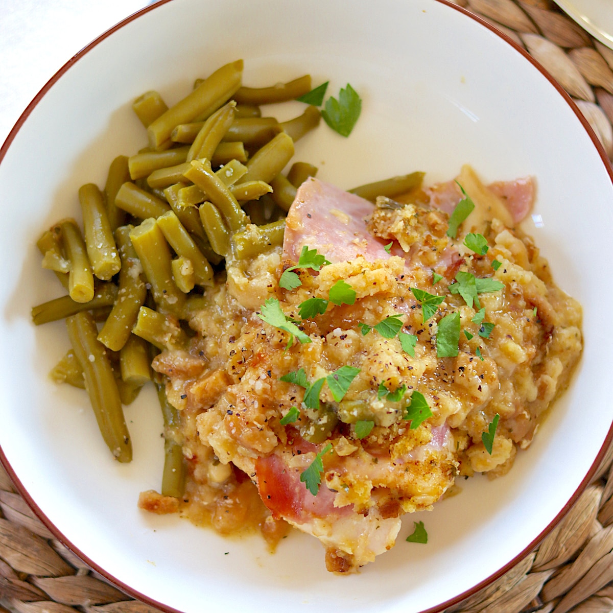 A brown rimmed white shallow bowl with chicken, ham, swiss cheese, and stuffing.