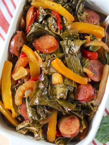 Colorful yellow peppers, andouille sausage, and collard greens in a white serving dish.