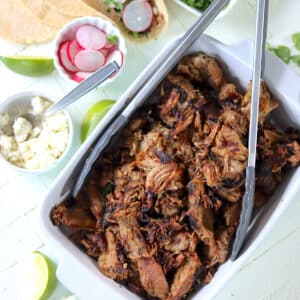 A white serving dish with crispy pulled pork pieces with cheese and radishes on the side.