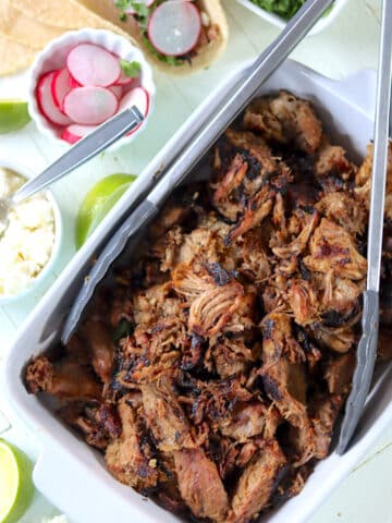 A white serving dish with crispy pulled pork pieces with cheese and radishes on the side.