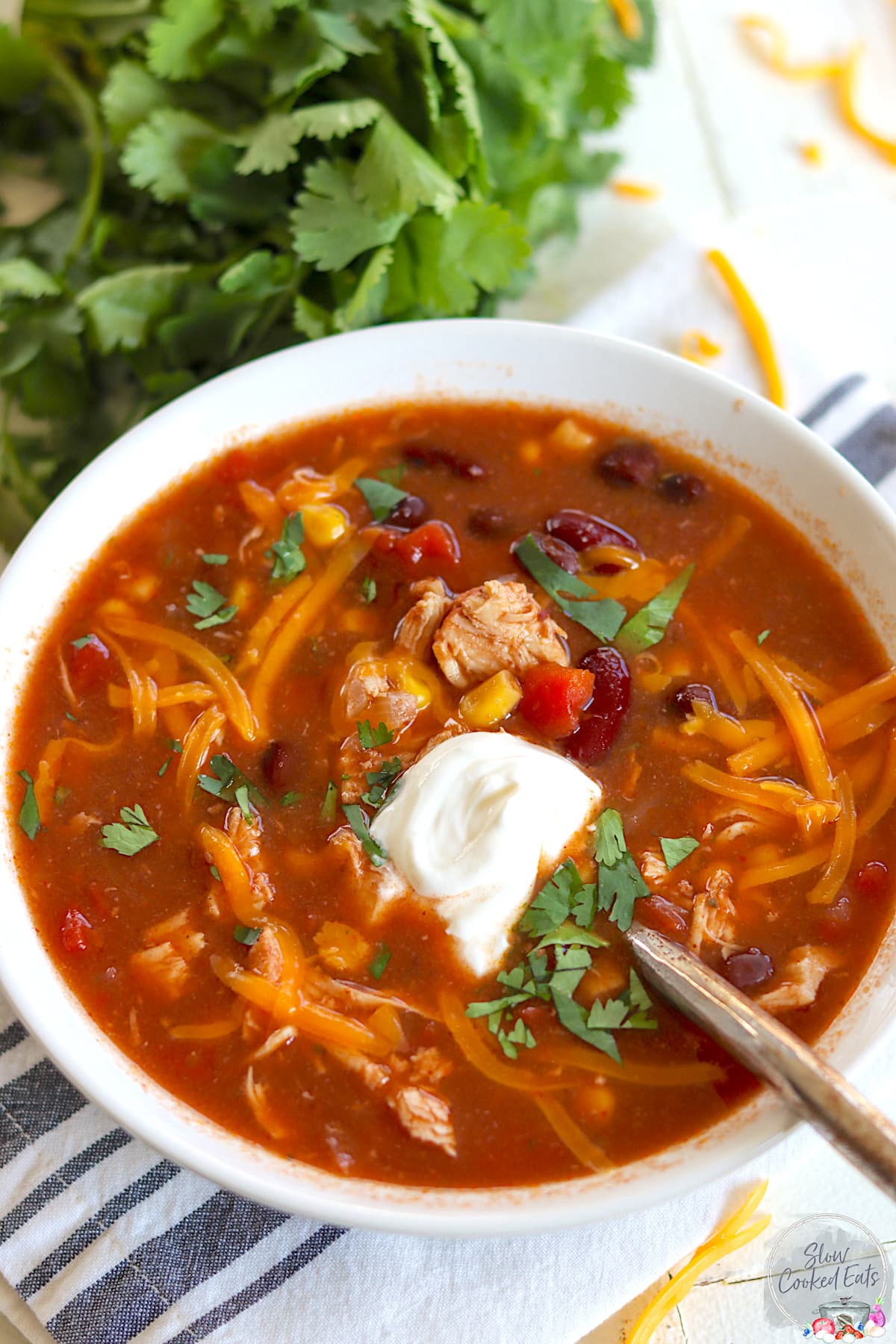 A white round bowl of slow cooker chicken taco soup garnished with cheddar cheese and fresh cilantro.