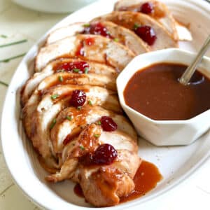 Slices of slow cooker boneless turkey breast on a white plate drizzled with cranberry gravy.