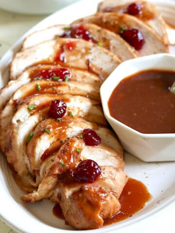 Slices of slow cooker boneless turkey breast on a white plate drizzled with cranberry gravy.