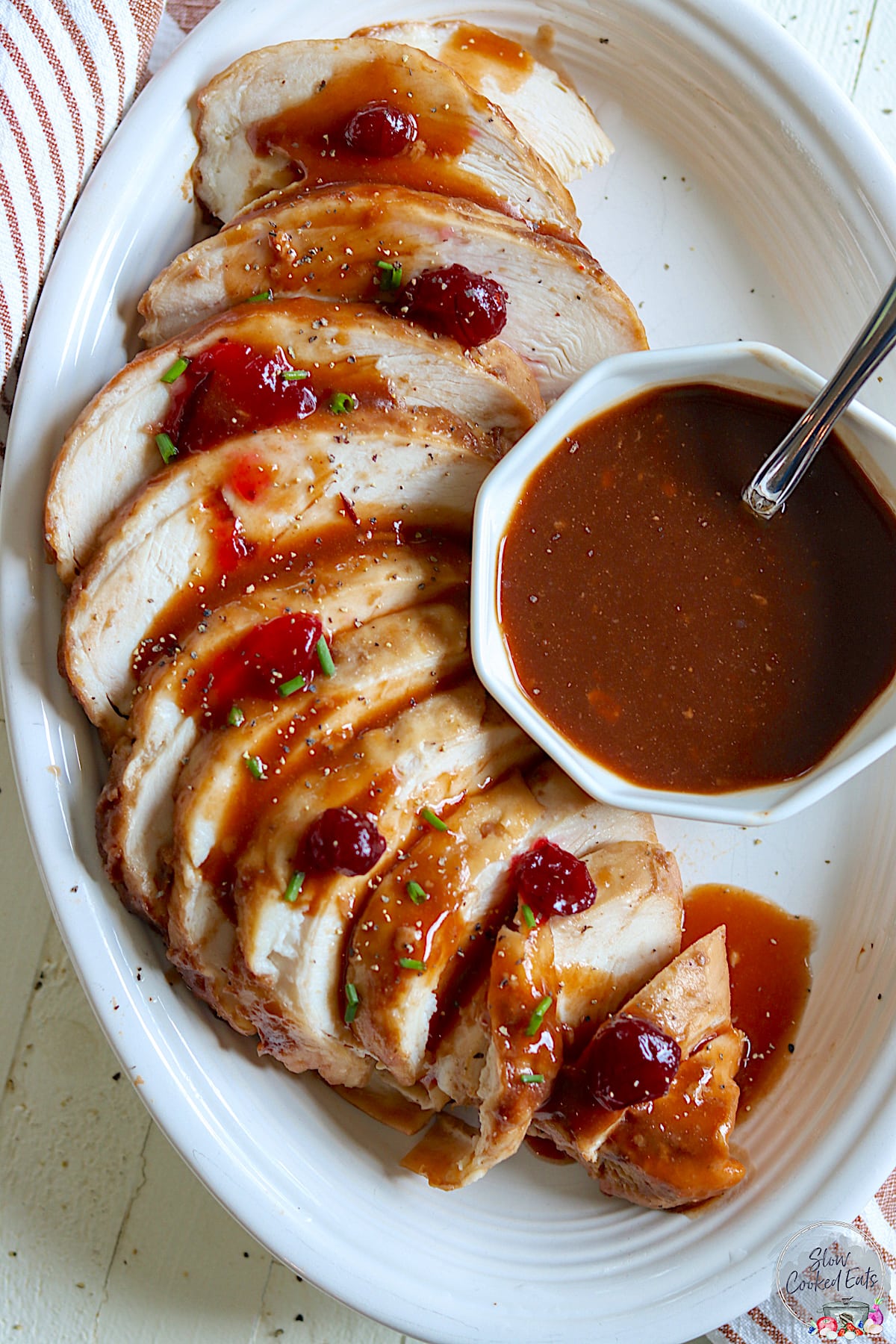 A sliced boneless turkey breast on a white plate drizzle with cranberry gravy.