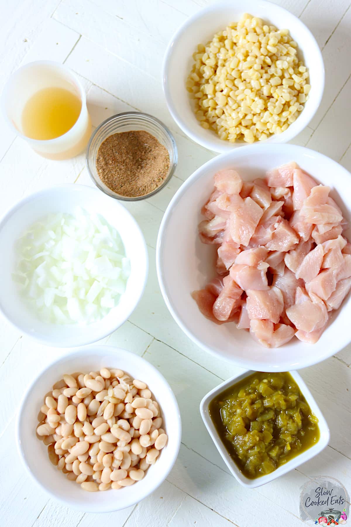 Ingredients needed for making slow cooker white chicken chili on a white wooden board.