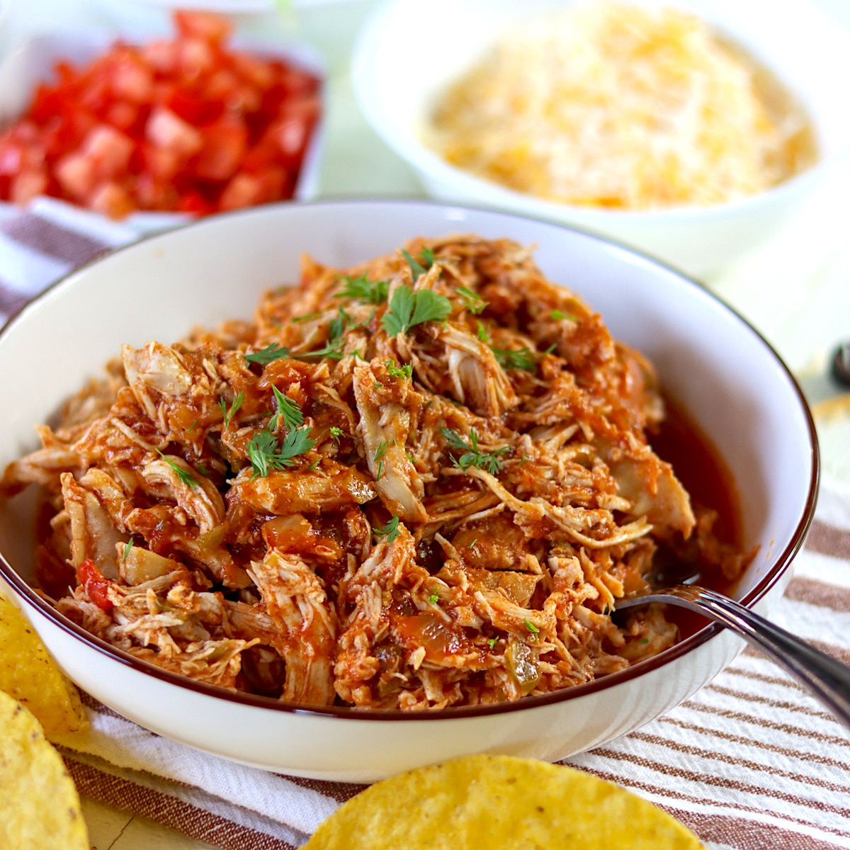 Slow cooked shredded chicken tacos filling piled in a white bowl and garnished with fresh cilantro.