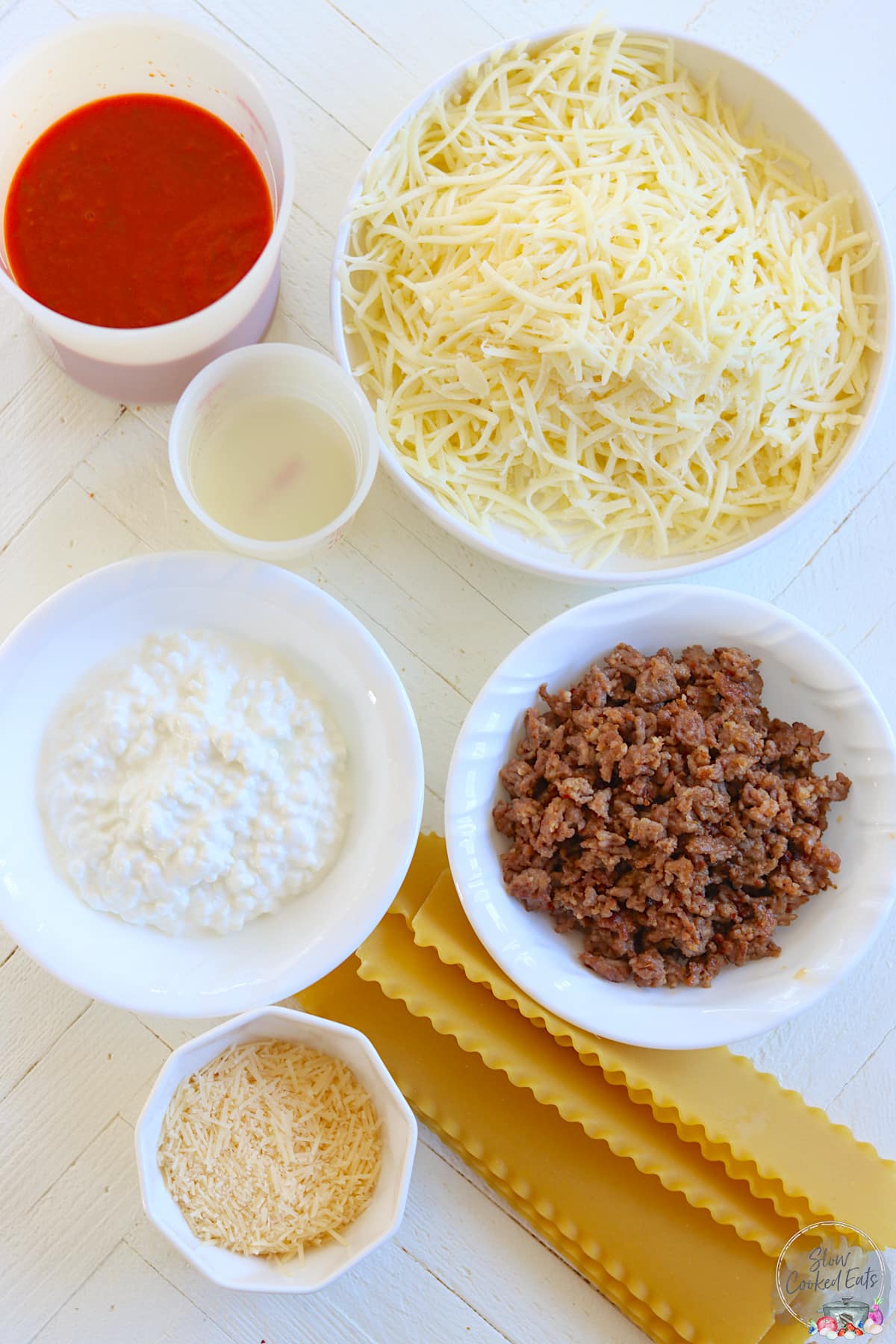 All the ingredients needed for making crockpot lasagna laying on a white wooden table.